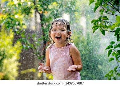 Happy Child Girl Playing Under The Rain. Family Have Fun Time Outdoors Under Summer Shower. Kid Without Umbrella Playing With Rain. Summer Holiday Concept.