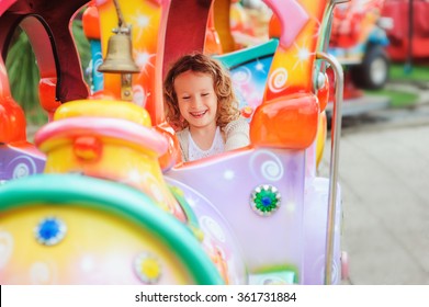 happy child girl riding train on funfair on summer vacation
