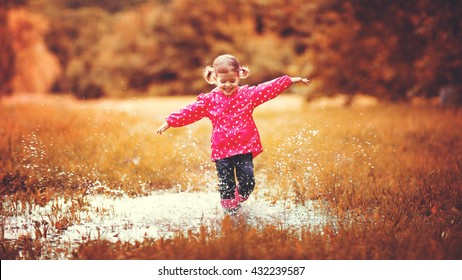 Happy Child Girl Running And Jumping In Puddles After Rain In Autumn