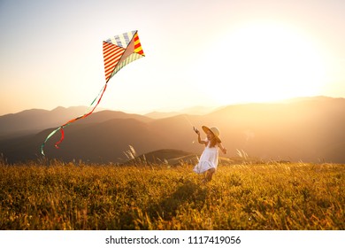 happy child girl running with a kite at sunset outdoors