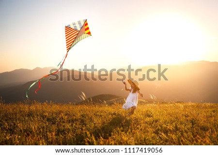 happy child girl running with a kite at sunset outdoors
