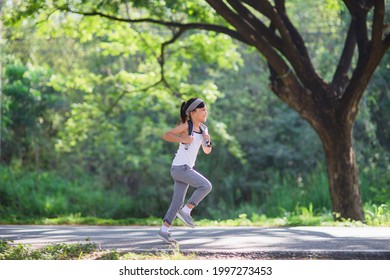 Happy Child Girl Running In The Park In Summer In Nature. Warm Sunlight Flare. Asian Little Is Running In A Park. Outdoor Sports And Fitness, Exercise And Competition Learning For Kid Development.