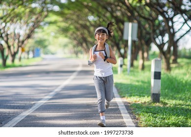 Happy Child Girl Running In The Park In Summer In Nature. Warm Sunlight Flare. Asian Little Is Running In A Park. Outdoor Sports And Fitness, Exercise And Competition Learning For Kid Development.