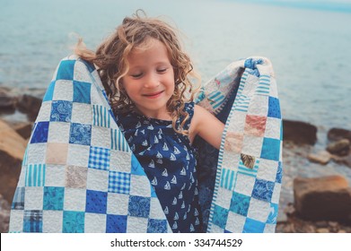 Happy Child Girl At Sea Wrapped In Quilt Blanket, Warm Cozy Mood On Summer Vacation