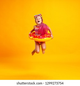 Happy Child Girl In Swimsuit With Swimming Ring Donut On A Colored Yellow Background
