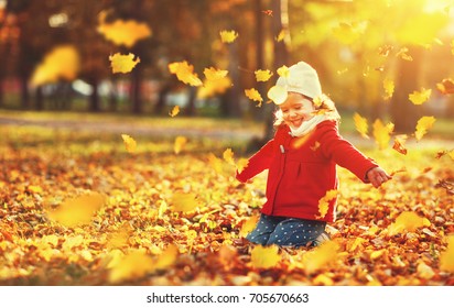 Happy Child Girl Throws Autumn Leaves And Laughs Outdoors
