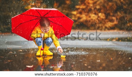 happy child girl with umbrella and paper boat in a puddle in   autumn on nature
