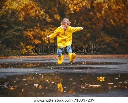 happy child girl with an umbrella and rubber boots in puddle on an autumn walk
