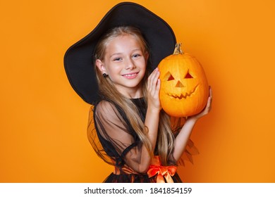 Happy child girl in witch costume holding pumpkin
