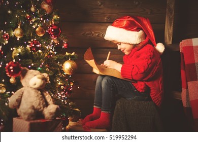 Happy Child Girl Writes Letter To Santa Claus At The Christmas Tree In The Evening