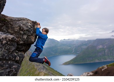 Happy child, hanging from a rock over Segla mountain on Senja island, North Norway. Amazing beautiful landscape and splendid nature in scandinavian country