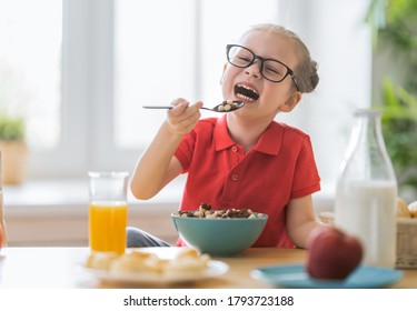 Happy child having breakfast. Kid eating cereal in kitchen.