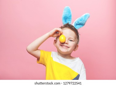 Happy Child Having Fun On Easter Egg Hunt. School Boy Wearing Bunny Ears  Holding Easter Egg On Pink Background. Stylish Kid With Colorful Eggs.