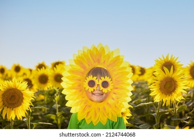 Happy child having fun in spring field of sunflowers. Outdoor portrait of funny kid against blue sky background