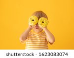 Happy child holding glazed donut. Portrait of funny kid against yellow background