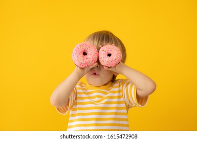 Happy child holding glazed donut. Portrait of funny kid against yellow background - Shutterstock ID 1615472908