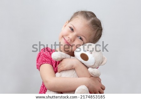Happy child hugging teddy bear on white background caucasian little girl of 5-6 years in red looking at camera
