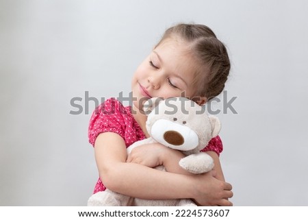 Happy child hugging teddy bear on white background caucasian little girl of 5-6 years in red with closed eyes