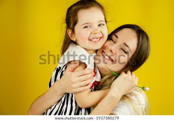 Happy child hugs mom. Strong hugs for children.\
Little daughter hugs mom. Happy mother with her baby on a yellow\
background. Hugs of mom and baby on a yellow background. A loving\
family.Family concept