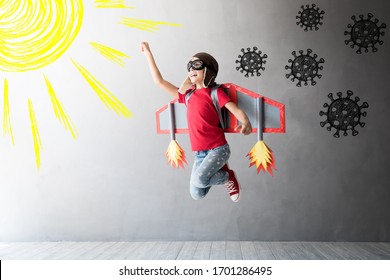 Happy Child Jumping With Toy Cardboard Wings. Kid Pilot Flying Away From Covid Virus. Sun And Vitamin D Concept