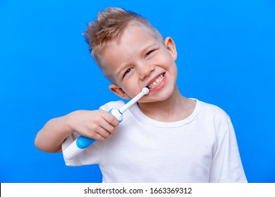 Happy child kid boy brushing teeth with electric toothbrush on blue background. Health care, dental hygiene. Mockup, copy space