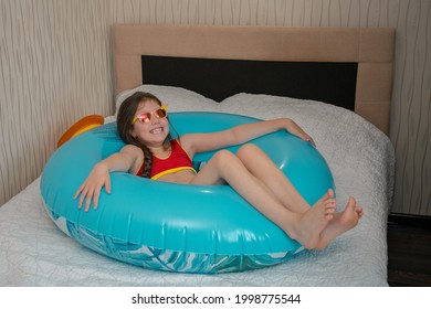 Happy Child Lies On An Inflatable Ring In The Bedroom. A Joyful Little Girl Is Resting On A Rubber Ring In Her Bed.