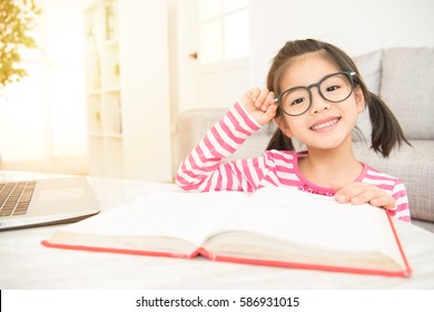 happy child little asian girl smile with holding glasses reading a books on the table in the living room at home. family activity concept.