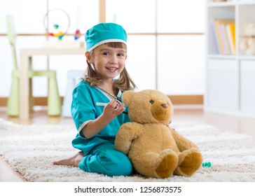 Happy Child Little Doctor Girl Examines Teddy Bear In Nursery Room At Home.