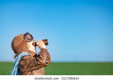 Happy child looking through binoculars outdoor in spring green field. Kid having fun against blue sky background. Imagination and freedom concept