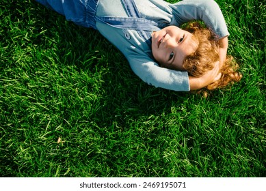 Happy child lying in grass from above. Little girl enjoy playing in green field. Smiling people background concept. Top view. - Powered by Shutterstock