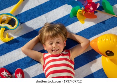 Happy Kind liegt auf gestreiftem Handtuch im Freien. Top-View-Portrait von Kind. Das lustige Baby lächelt. Sommerurlaubskonzept