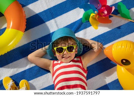 Happy child lying on striped towel outdoor. Top view portrait of kid. Funny baby smiling. Summer vacation concept