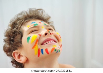Happy child painted colorful stripes on his face with paints. 