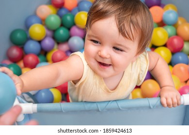 Happy Child In The Play Pool With Colorful Balls. The Baby Holds The Ball To The Parent