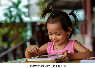 Happy child playing with her tablet outdoors on the table during relax time.