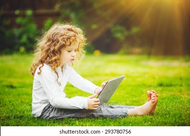 Happy child playing laptop sitting on the grass.