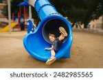 Happy Child Playing on Blue Slide in Playground