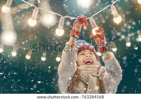 Happy child playing on a snowy winter walk. Little girl enjoying the holidays. Portrait kid on dark background.