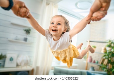 Happy Child Is Playing With Parent At Home. Father Is Spinning With Daughter.