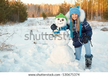 happy child playing with snowman. funny girl on a walk in the winter outdoors