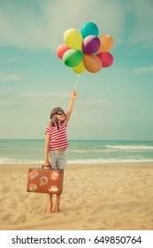 Happy child playing with toy air balloons against sea and sky background. Kid pilot having fun outdoor. Summer vacation and travel concept. Freedom and imagination