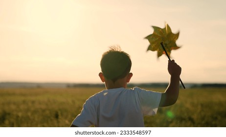 Happy child playing with toy pinwheel outdoors in summer in park against blue sky. Child boy runs with toy wind turbine in his hand on summer field, sun day. Childhood children. Family holiday, nature - Powered by Shutterstock