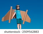 Happy child playing with toy wings against summer sky. Kid dreams of future. Kid pilot dreaming. Childhood dream concept. Blonde cute daydreamer child dream on fly. Dreams and imagination.