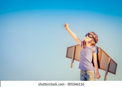 Happy child playing with toy wings against summer sky background