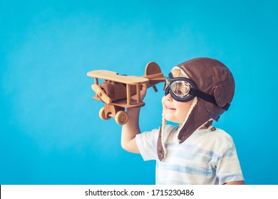Happy child playing with vintage wooden airplane. Kid having fun against blue background. Imagination and freedom concept
