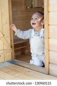 Happy Child Playing In A Wooden Playhouse Or A Small Garden Shed, Kneeling At The Door Looking Up.