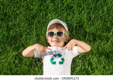 Happy child points fingers at recycle sign on t-shirt. Funny kid against spring green background. Ecology and Earth day concept. Top view - Powered by Shutterstock