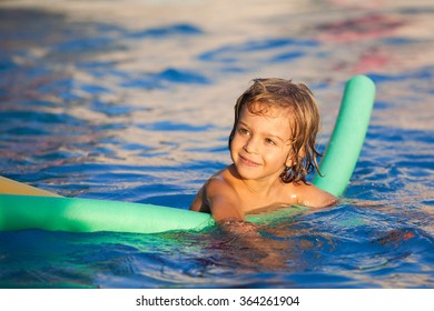 Happy Child In The Pool, Learning To Swim With Swimming Noodle; Warm Sunset Light