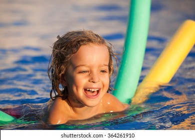 Happy Child In The Pool, Learning To Swim With Swimming Noodle; Warm Sunset Light