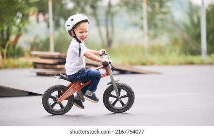 Happy child riding balance bike. Male toddler kid in helmet learning to ride on run bicycle at skate park.